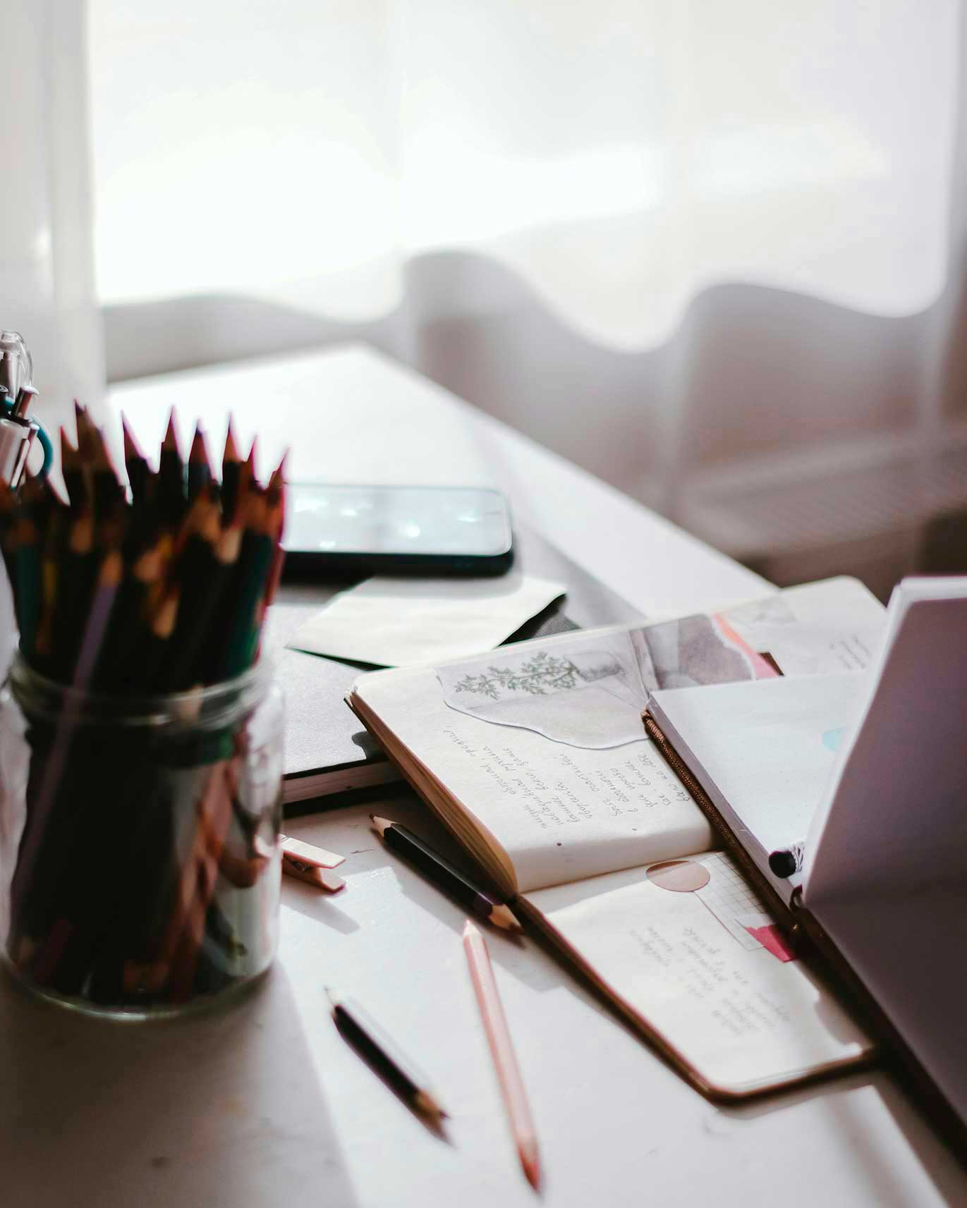 Journals and pens by an open window with curtains and morning light